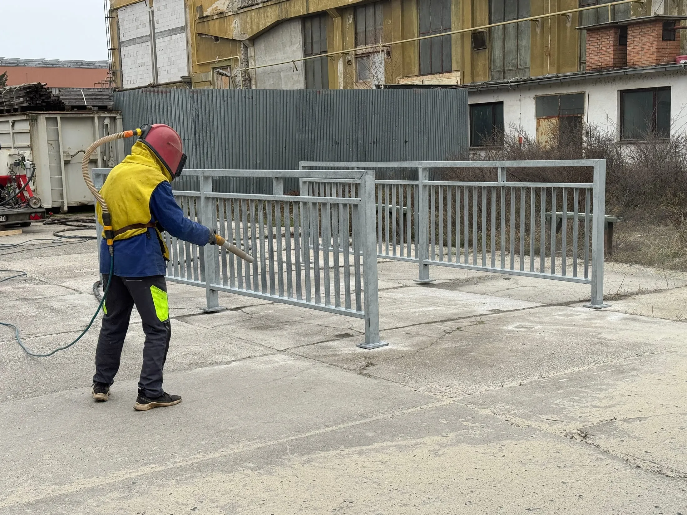 Pracovník pri sweep otryskávaní pozinkovaného zábradlia.